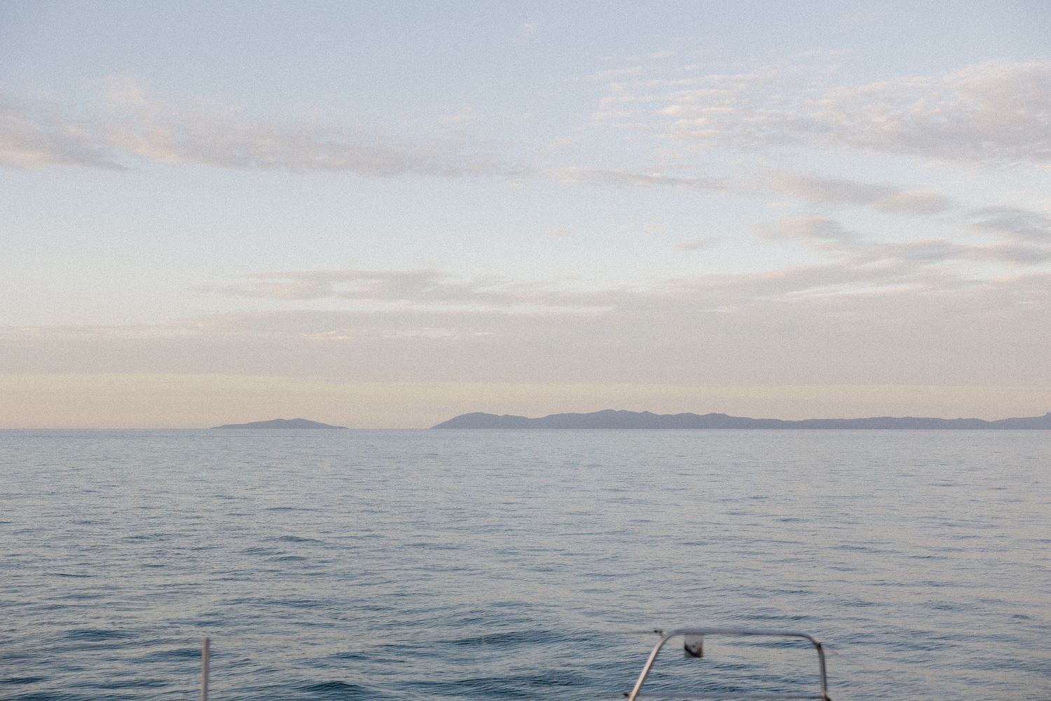 Tranquil seascape with distant islands viewed from a boat deck at dusk.