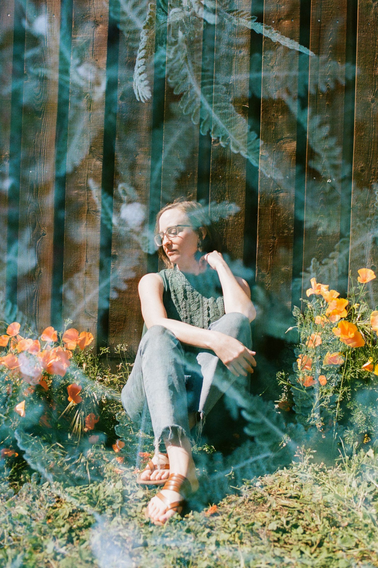 Naomi Boyer sits against a wall. Photo is double-exposed with flowers overlaying it.