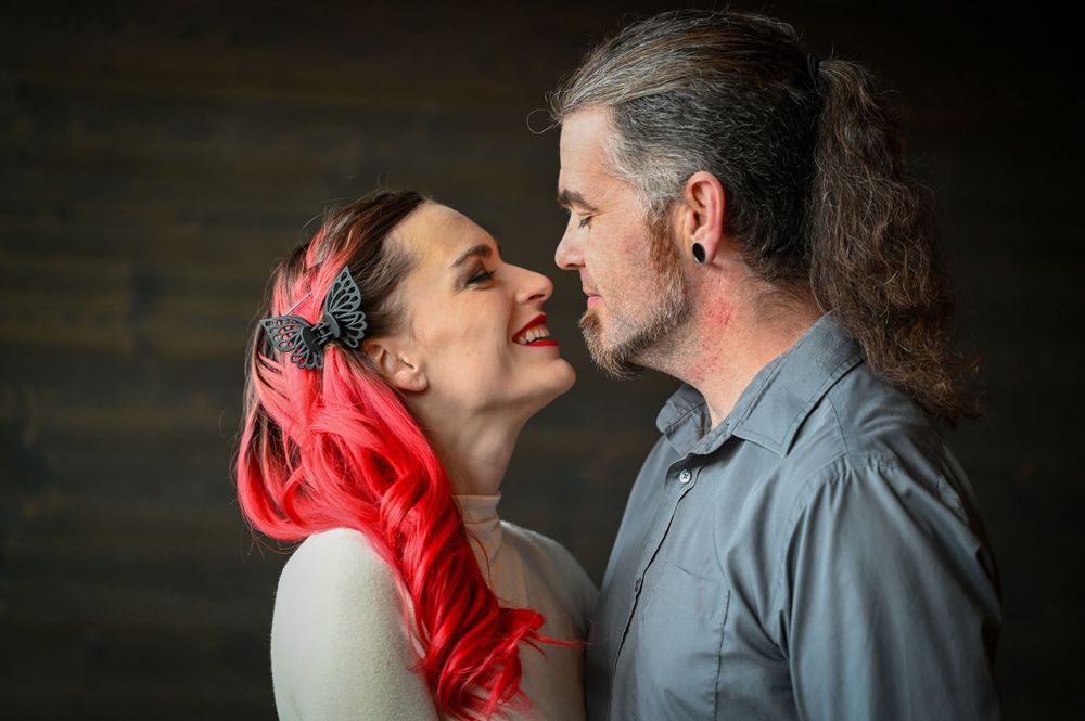 Couple with woman having bright pink hair sharing a tender moment, nearly kissing in a warmly lit setting.