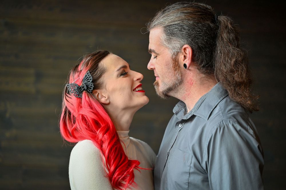 Couple with vibrant red hair leaning in for a kiss in a moody dark wood backdrop portrait.