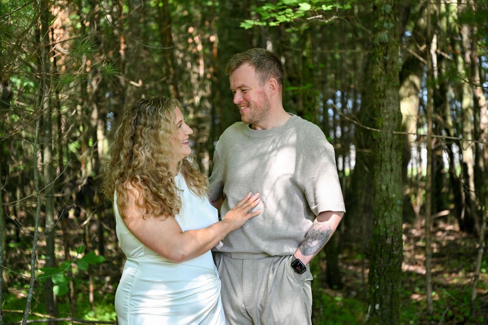 Couple sharing a tender moment in a lush green forest, smiling at each other on a sunny day.
