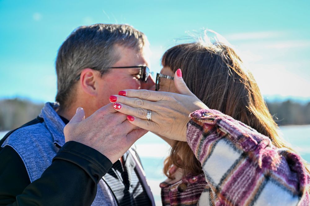 Couple sharing a romantic kiss outdoors in winter, woman displaying a diamond engagement ring on her hand.