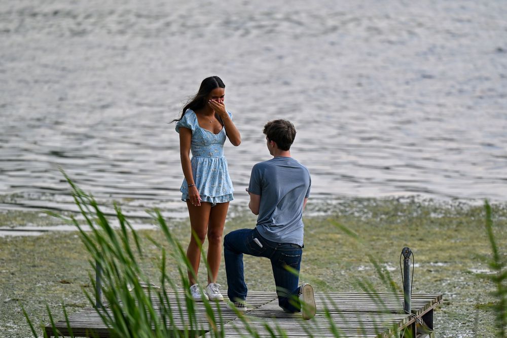 Emotional marriage proposal moment on a wooden dock beside a calm lake with lush greenery.