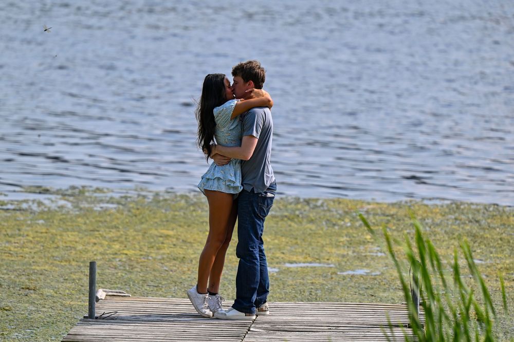 Romantic couple kissing on a lakeside dock surrounded by green algae-covered water.