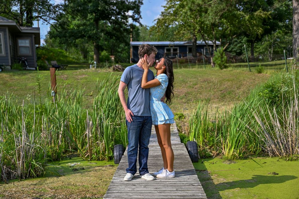 Couple sharing a kiss on a wooden boardwalk surrounded by lush green wetland vegetation.