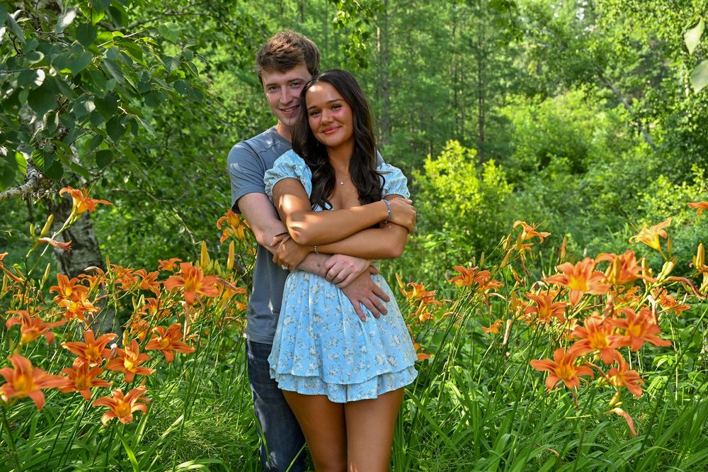 Happy couple embracing among vibrant orange daylilies in a lush garden.