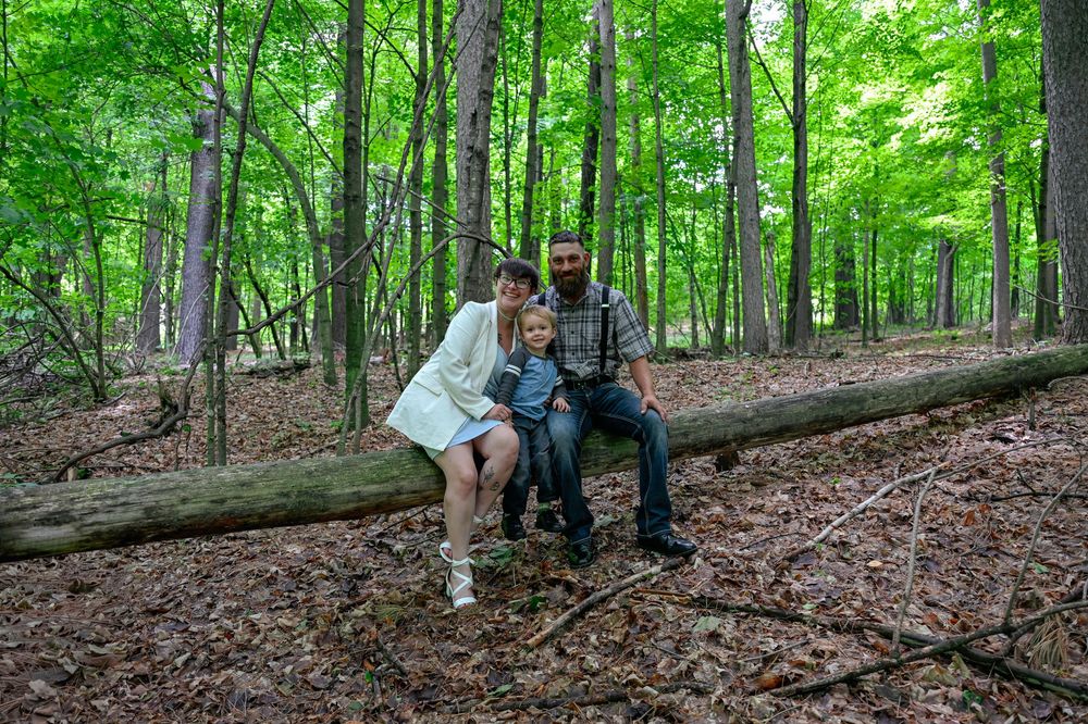 Family of three sitting on a fallen log in a dense green forest during summer.