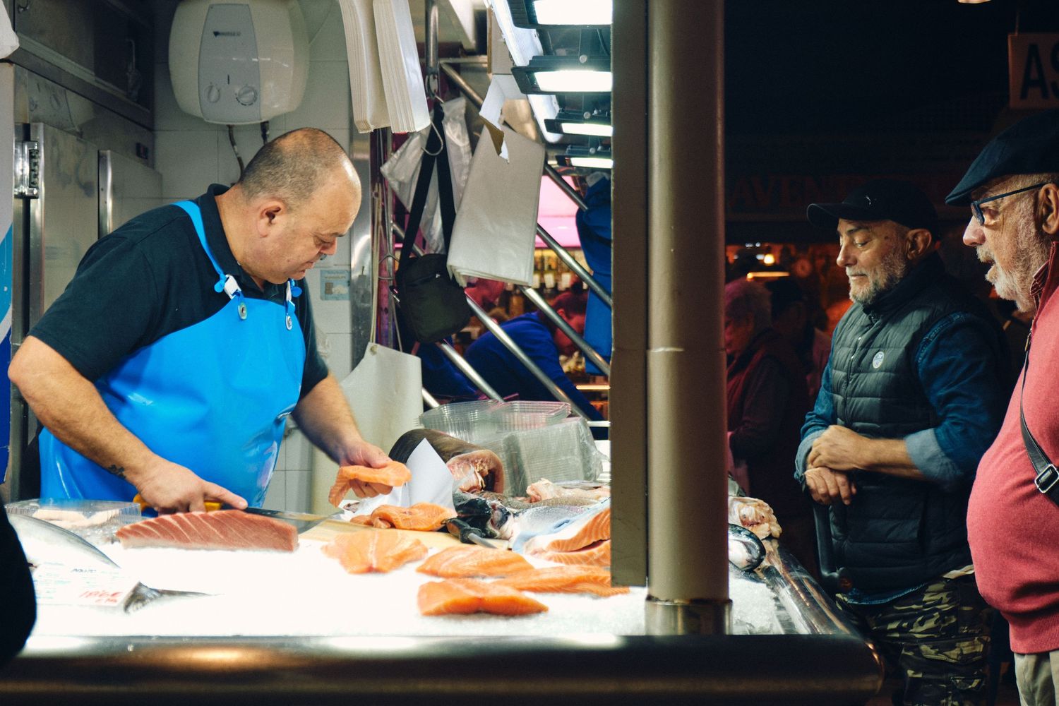 Fish vendor preparing fresh salmon at market counter while customers watch.