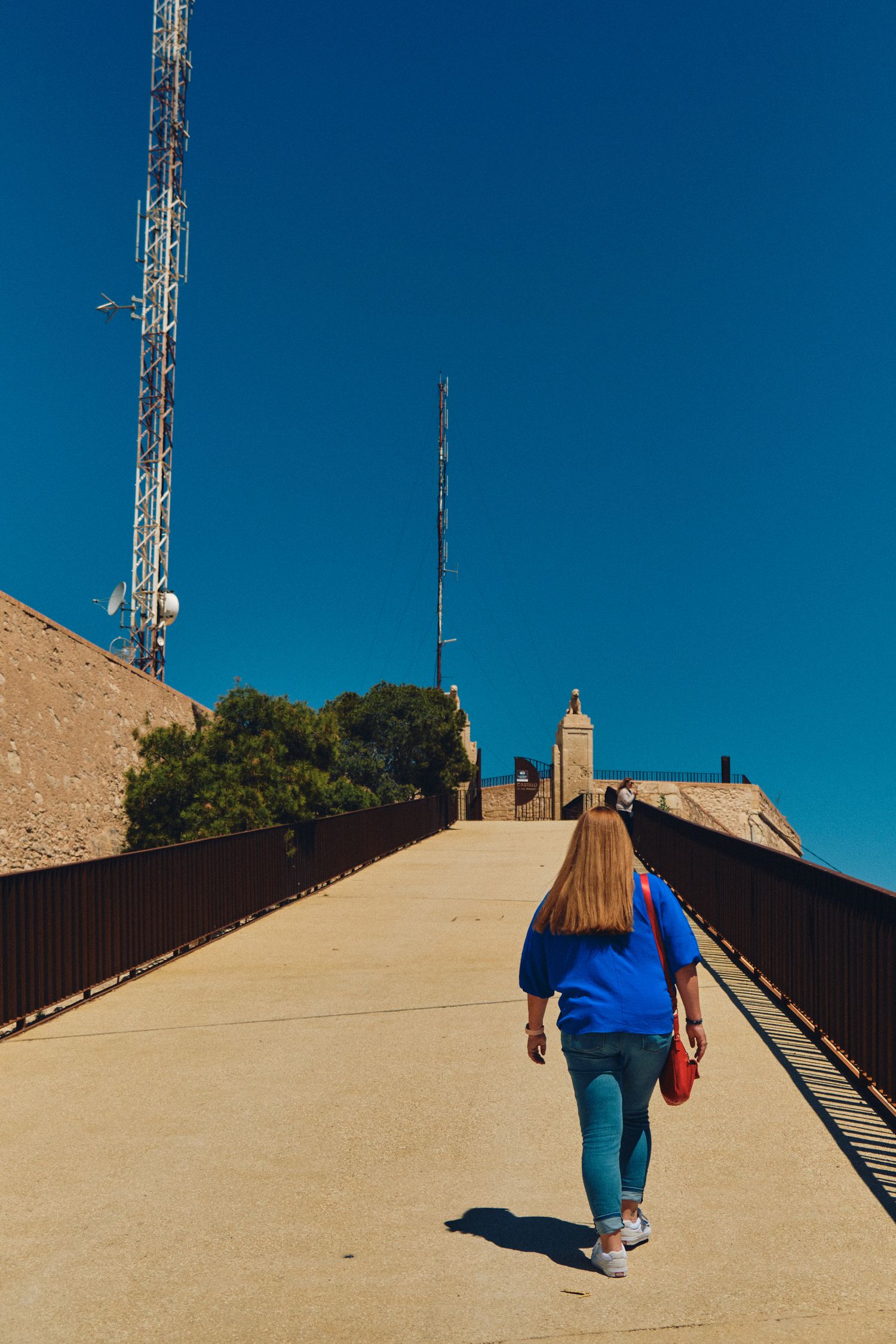 Person in blue walking up pathway towards communication towers on hilltop.