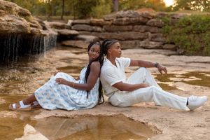 Two people in white dresses lay on sandy ground during golden hour sunset at a scenic outdoor location.