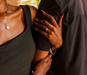 Close-up of a couple embracing, woman wearing a diamond engagement ring, bracelet, and necklace.