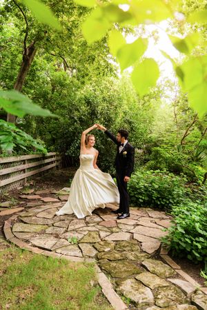 Bride and groom dancing on a stone patio surrounded by lush green gardens during an outdoor wedding ceremony.