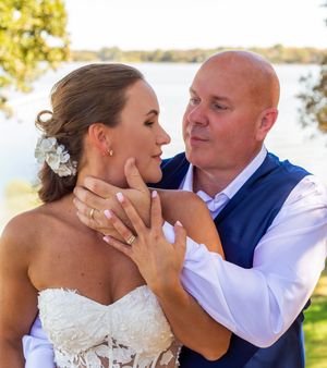 A romantic wedding moment captured outdoors by a lake with warm sunlight and natural scenery in the background.