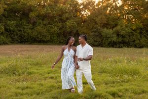 Couple in white outfits walking through a sunlit meadow at golden hour, creating a romantic outdoor scene.
