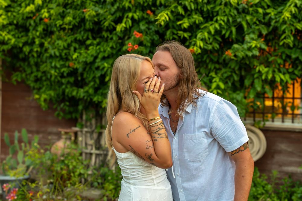 A couple shares a tender romantic moment in a lush garden setting during summer. (Proposal - Fortunata Winery Aubrey, TX)
