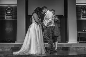 Black and white photo of a bride in a wedding gown standing with someone on a covered porch for an intimate ceremony.