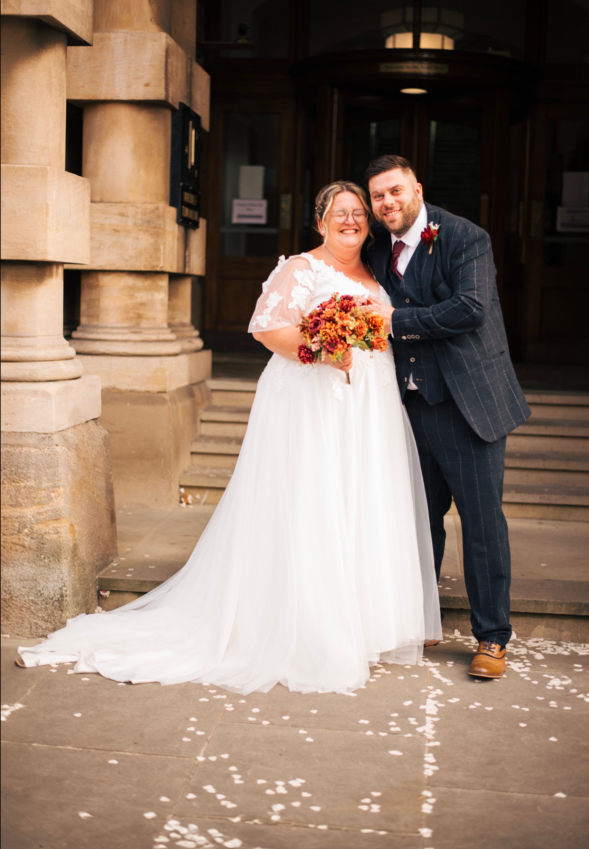 Wedding couple stands together on stone steps holding an autumn bouquet.