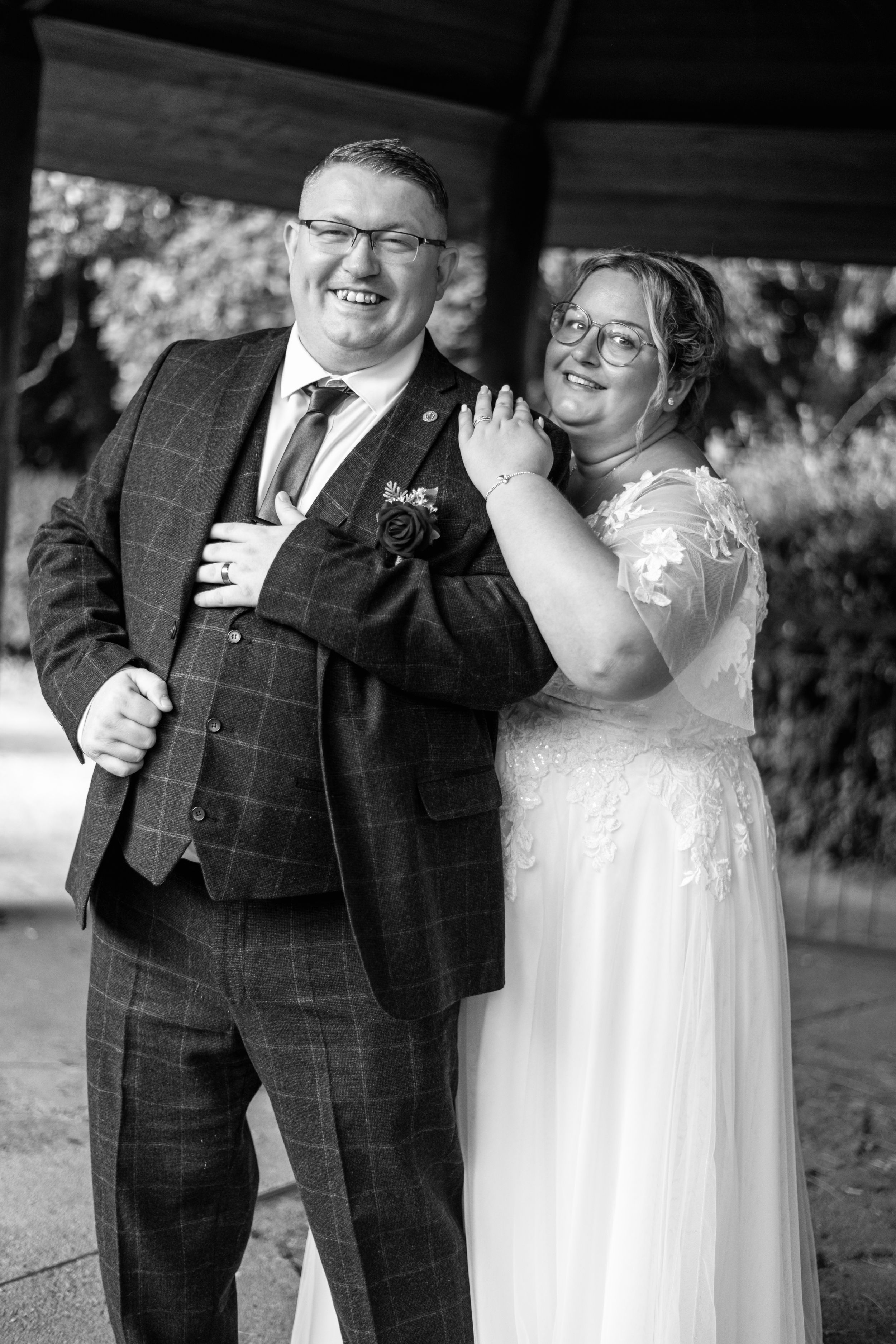 Black and white portrait showing couple in elegant wedding attire under outdoor shelter.