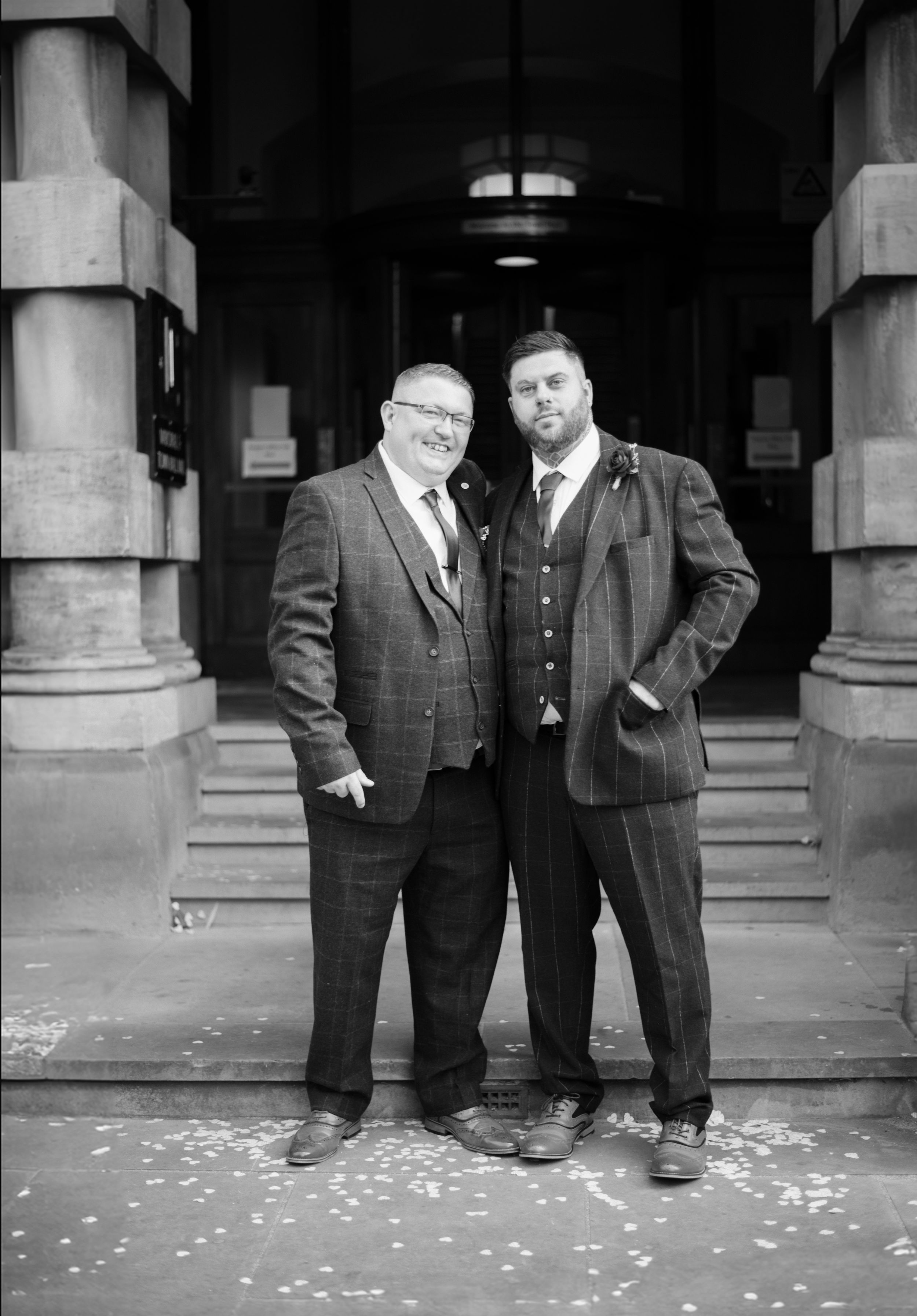 Two people in suits pose on stone steps outside a historic building entrance.