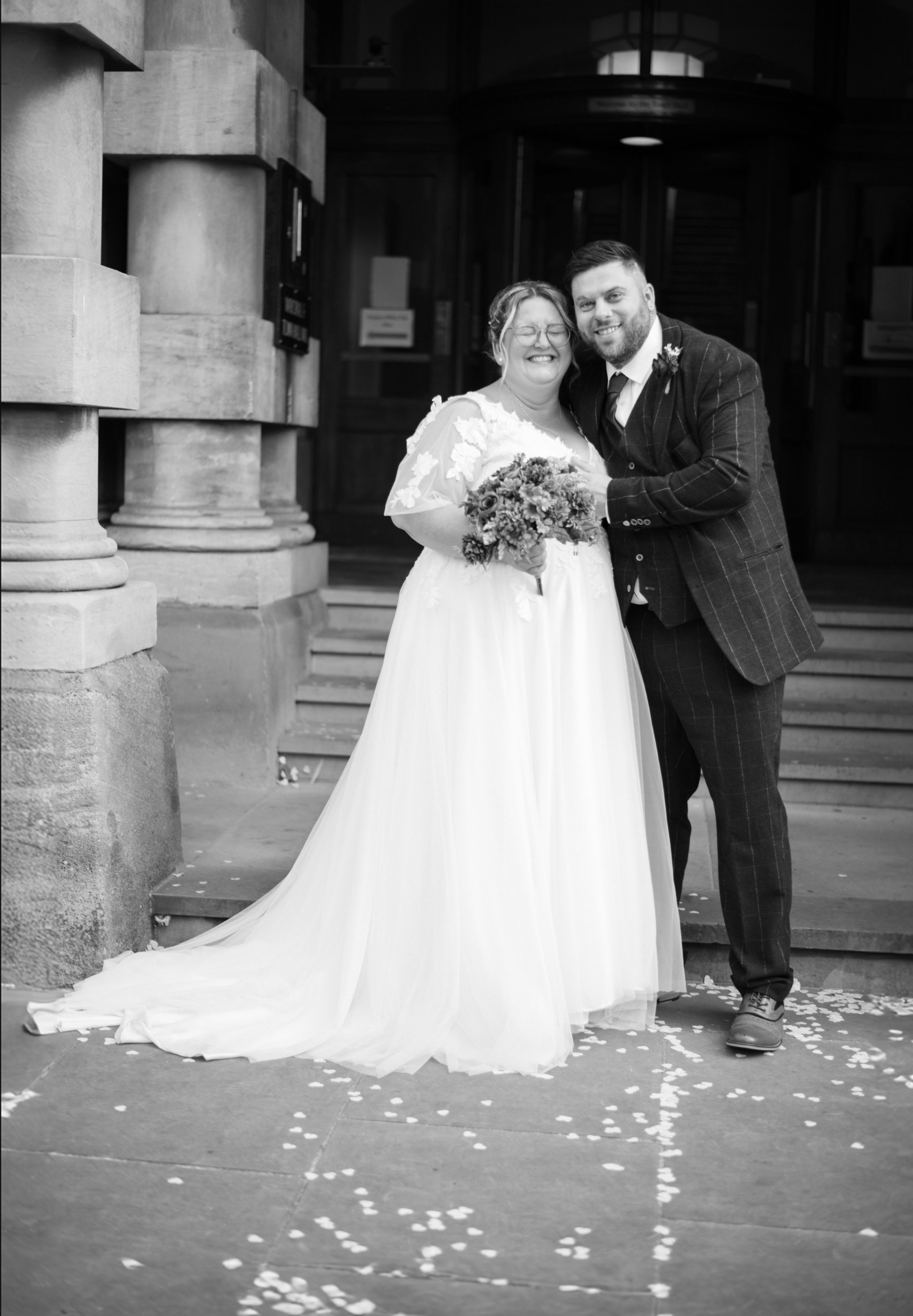 Newlyweds pose outside a historic stone building entrance.