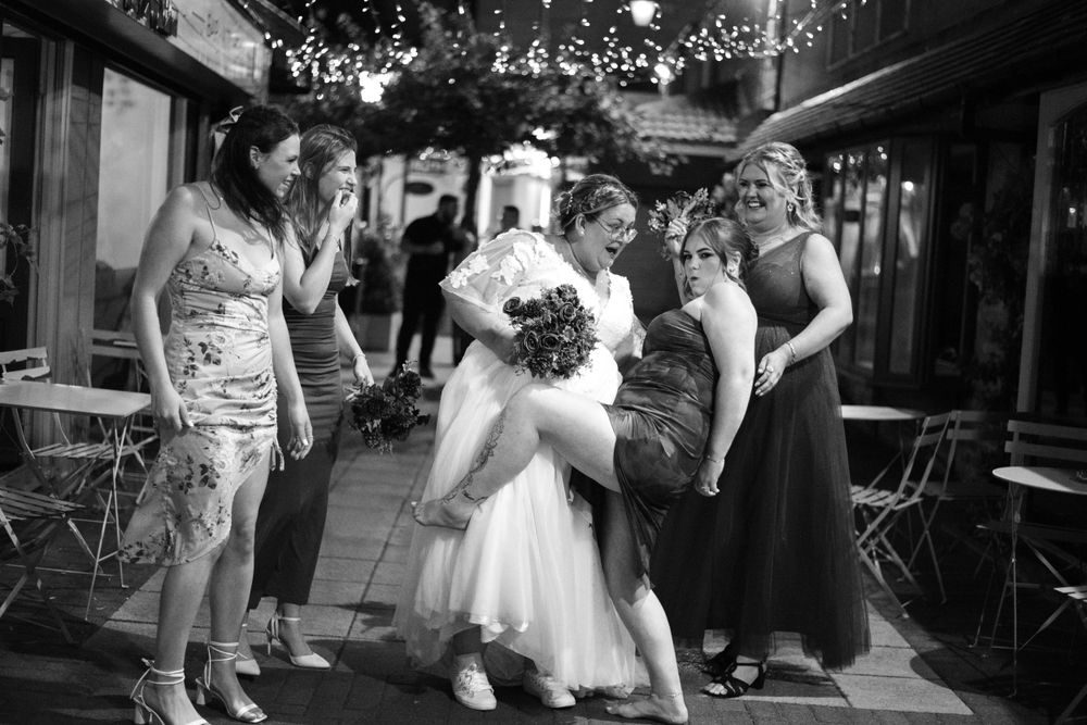 Wedding party gathers on a patio under string lights for a group photo.