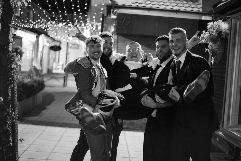 A group celebrates at an outdoor venue decorated with string lights in black and white.