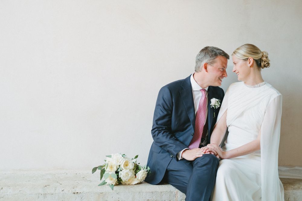 Intimate wedding portrait of couple seated together with white floral bouquet.