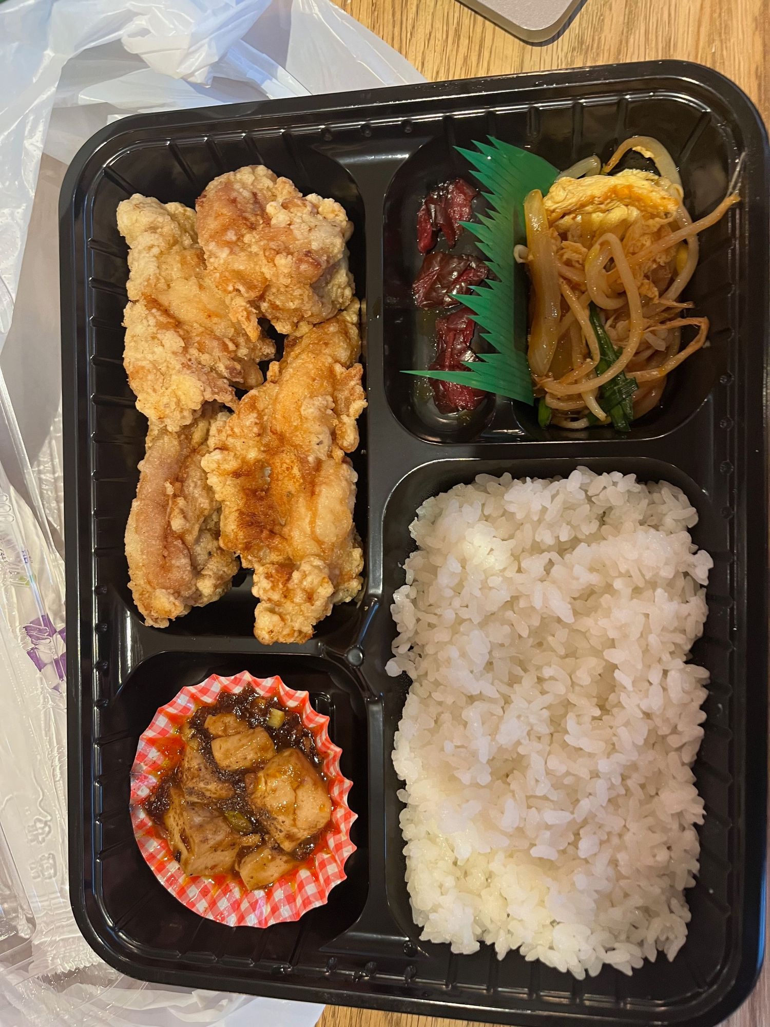 Japanese bento boxes with fried chicken, rice, and side dishes arranged in black containers.