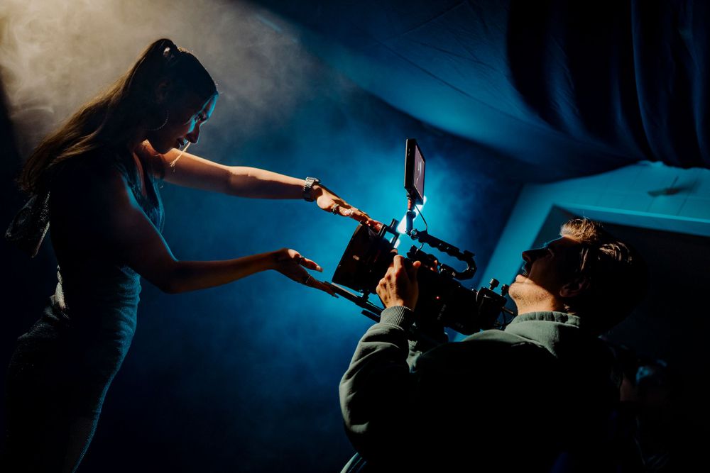 Behind the scenes shot of film crew working with camera equipment in dark blue lighting.