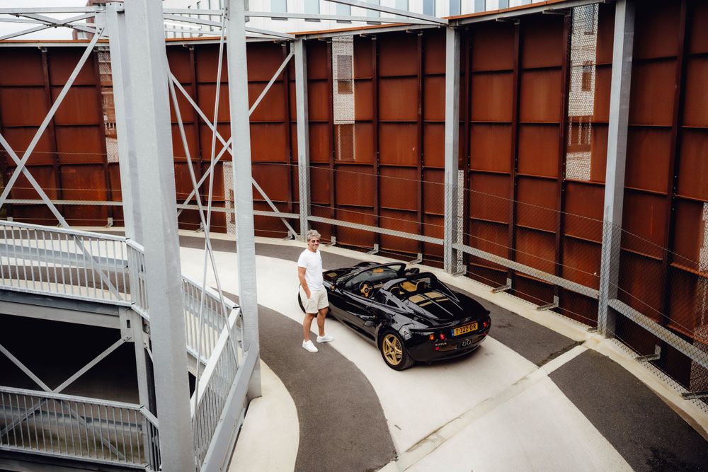 Black car driving through curved concrete parking structure with white support beams and orange walls.