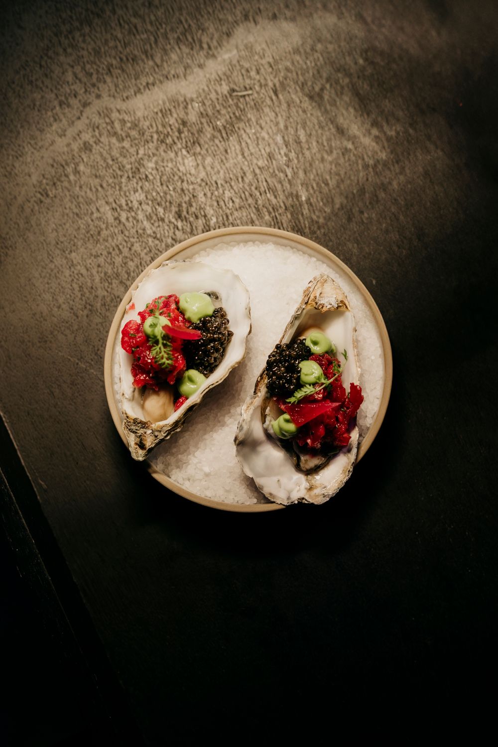 Gourmet oysters garnished with berries and microgreens on a textured plate.