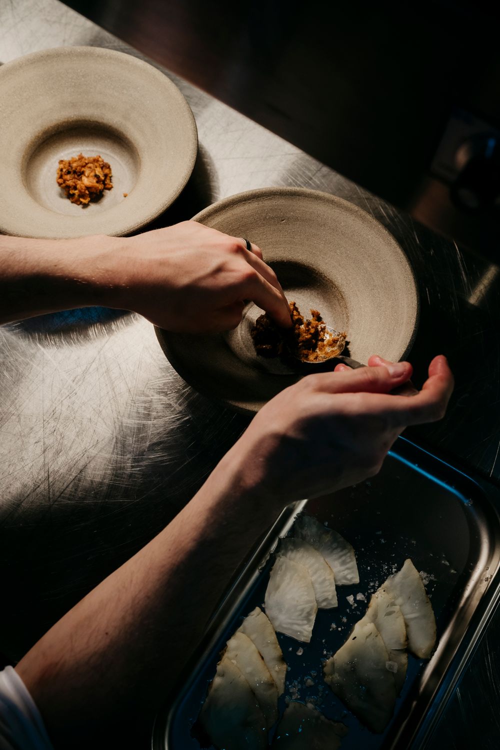 Hands plating food on ceramic dishes in moody, dramatic lighting.