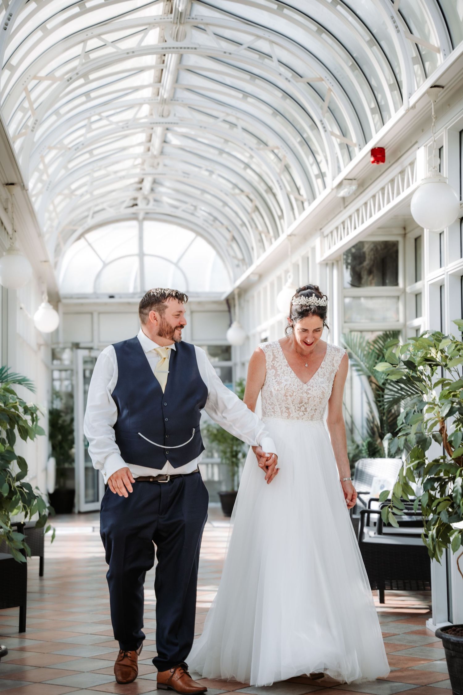 Couple dancing in an elegant white-arched conservatory with natural light streaming through.
