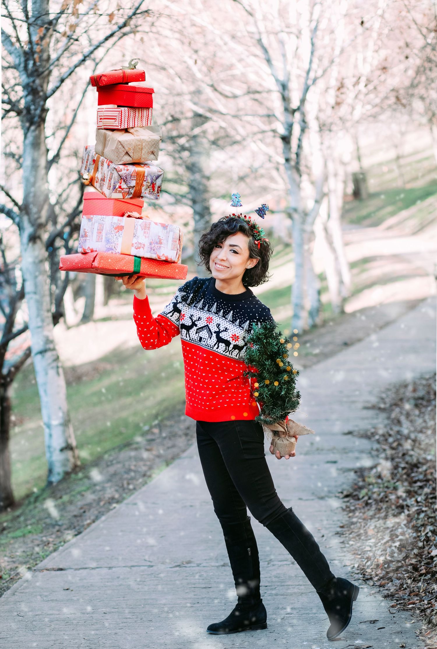 Person in festive red sweater balancing stack of wrapped Christmas presents on winter path.