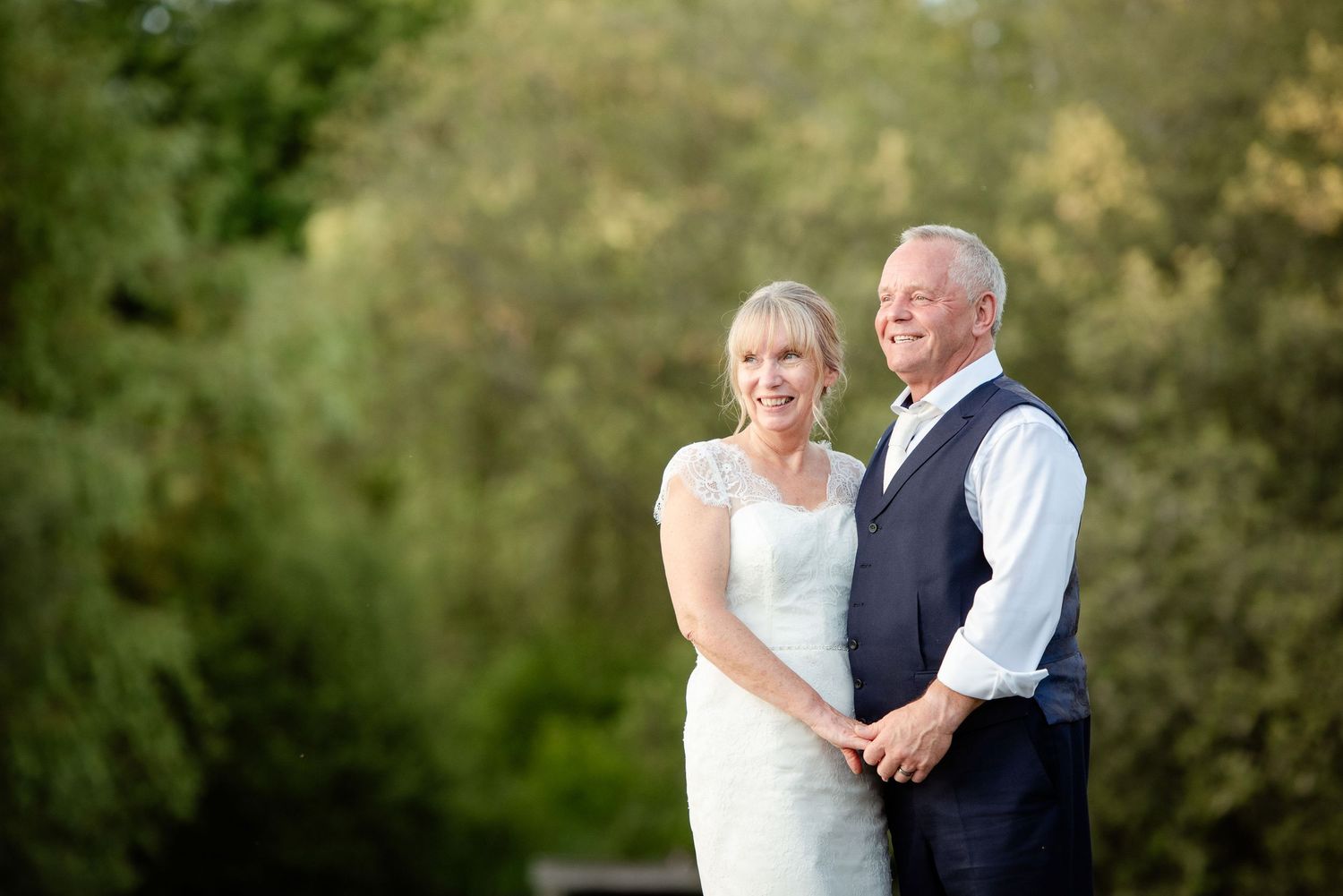 A romantic outdoor wedding portrait of a couple smiling together against a natural green background.