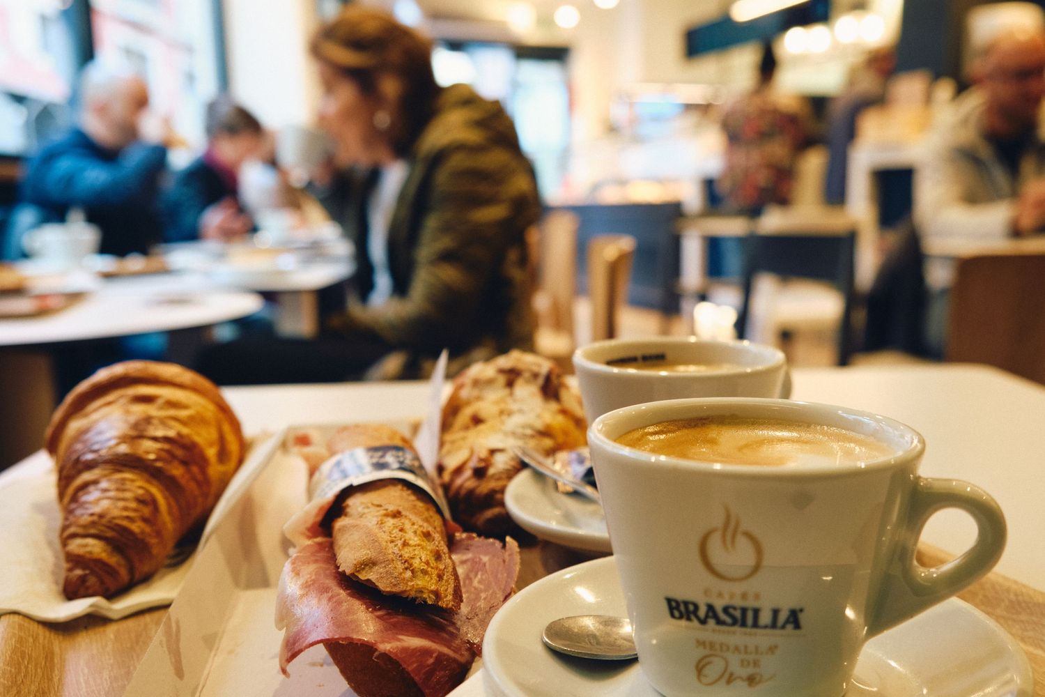 Fresh croissant and coffee served with other breakfast pastries on a cafe table.