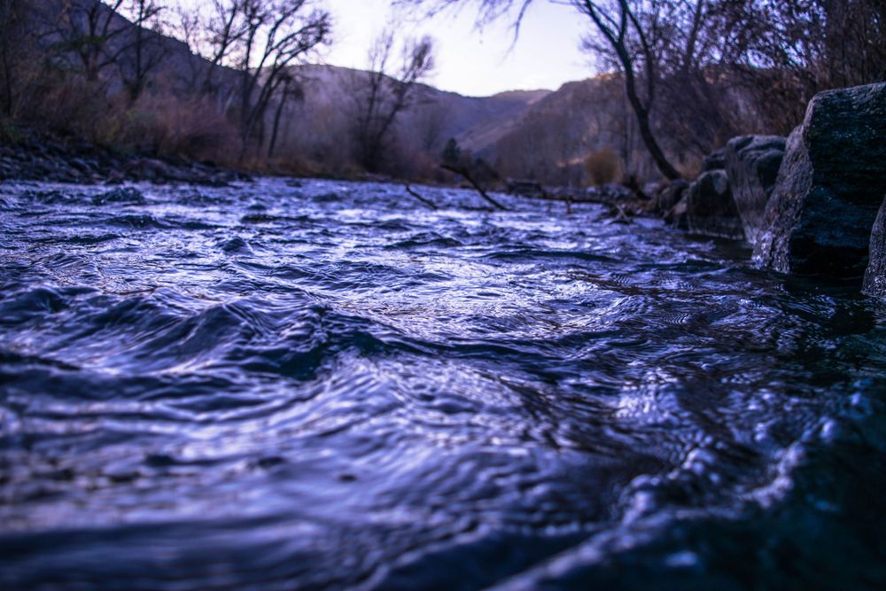 Flowing river water with ripples at dusk surrounded by mountains.