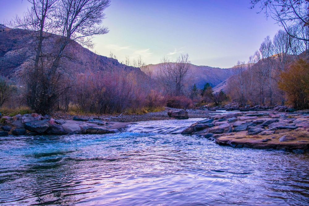 Scenic mountain stream flows over rocks at dusk with purple mountains in the background.