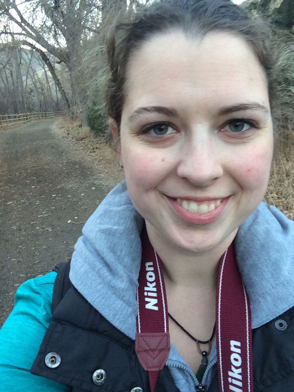 A nature enthusiast with a camera takes a selfie on a hiking trail.
