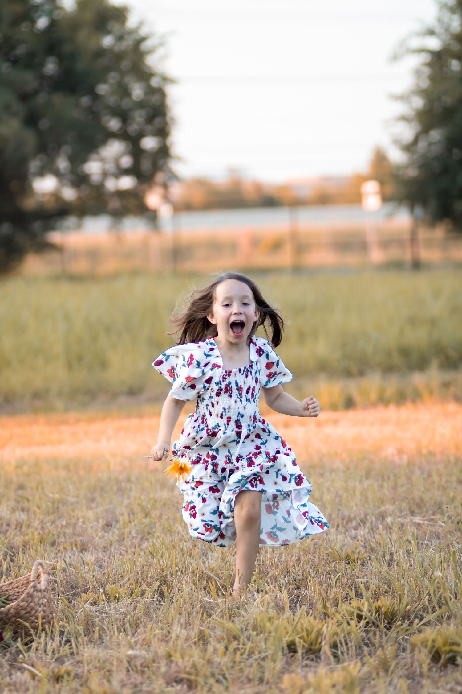 Playful child running and jumping through a sunlit field wearing a floral dress.