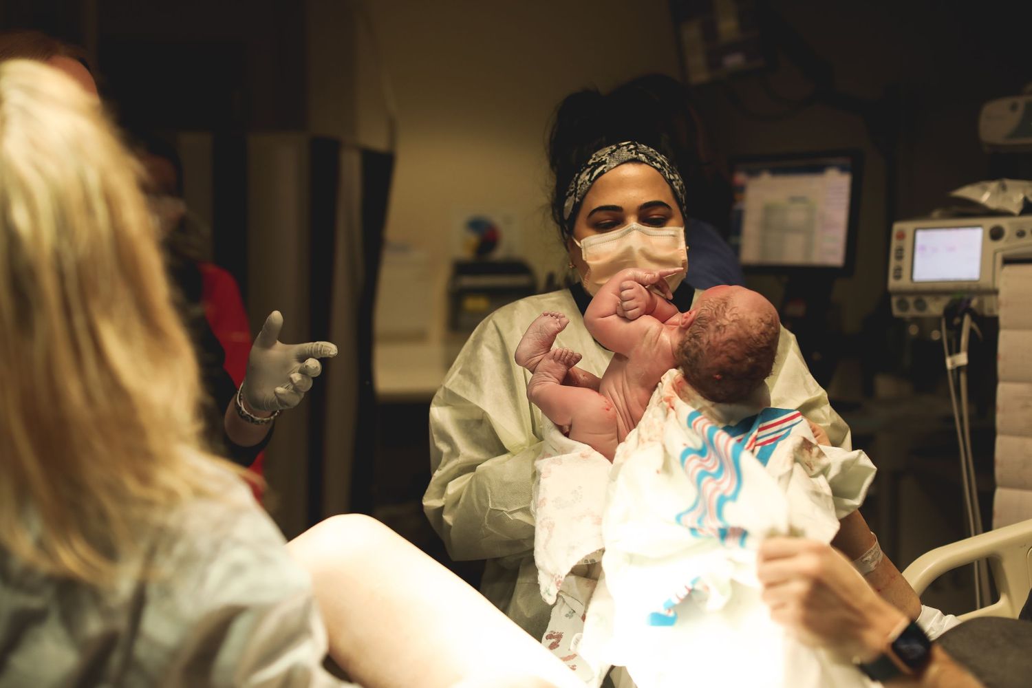 Medical staff attending to newborn in dimly lit hospital environment.