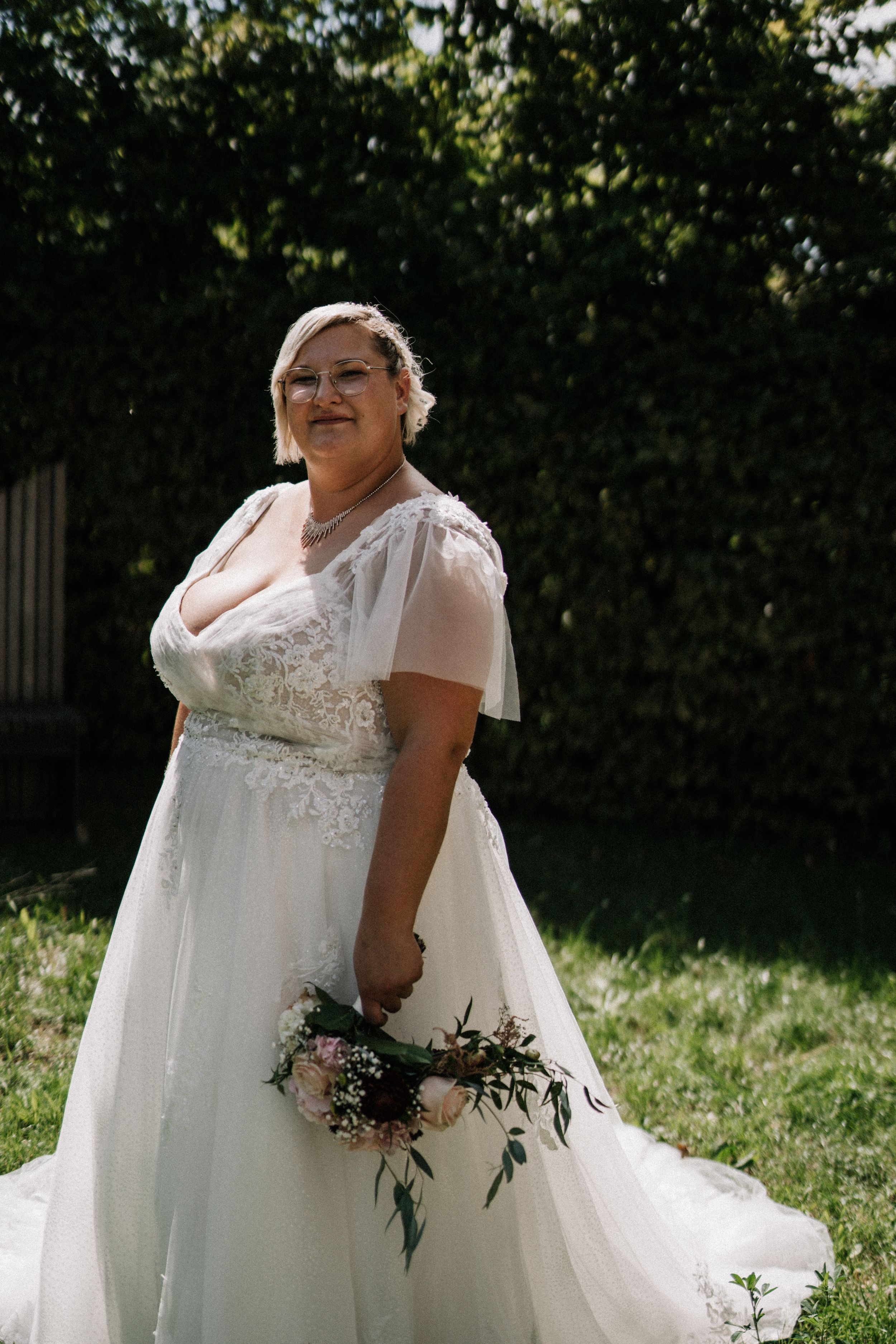 Elegant bride in cap sleeve wedding gown poses in a garden setting.