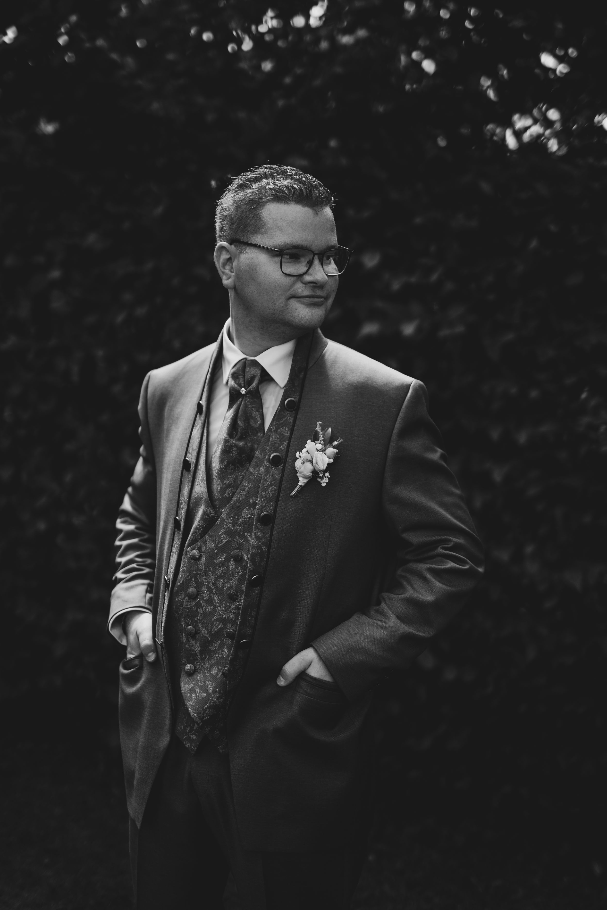 Black and white portrait of groom in formal suit with patterned vest and boutonniere.
