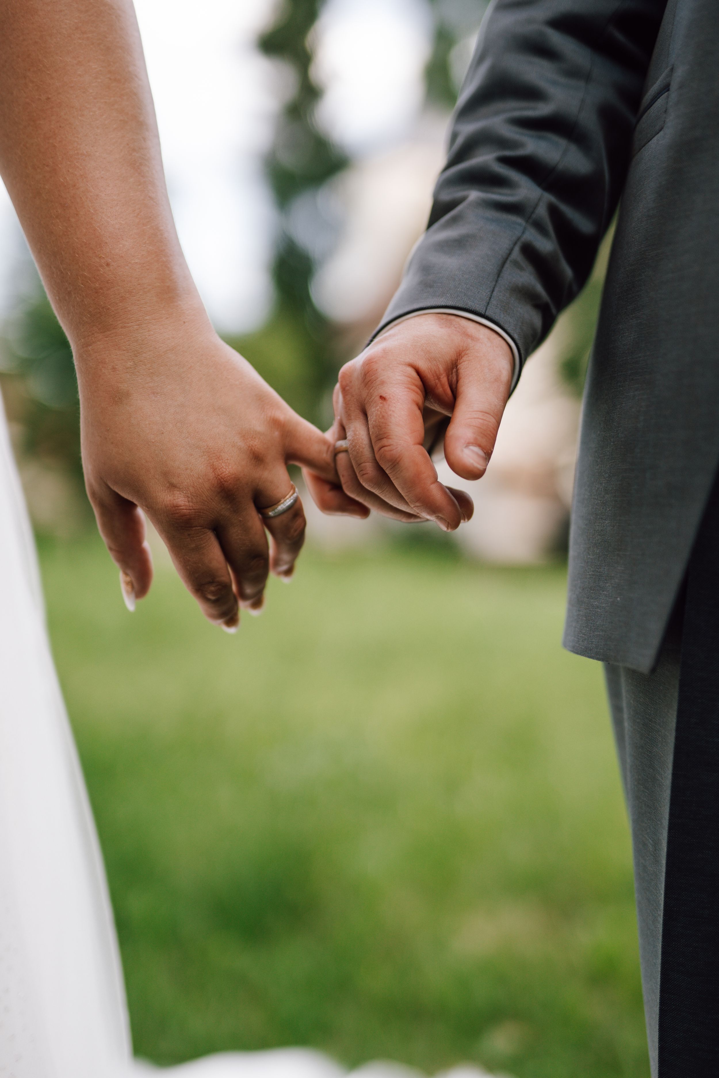 Close-up of newlyweds holding hands tenderly outdoors.