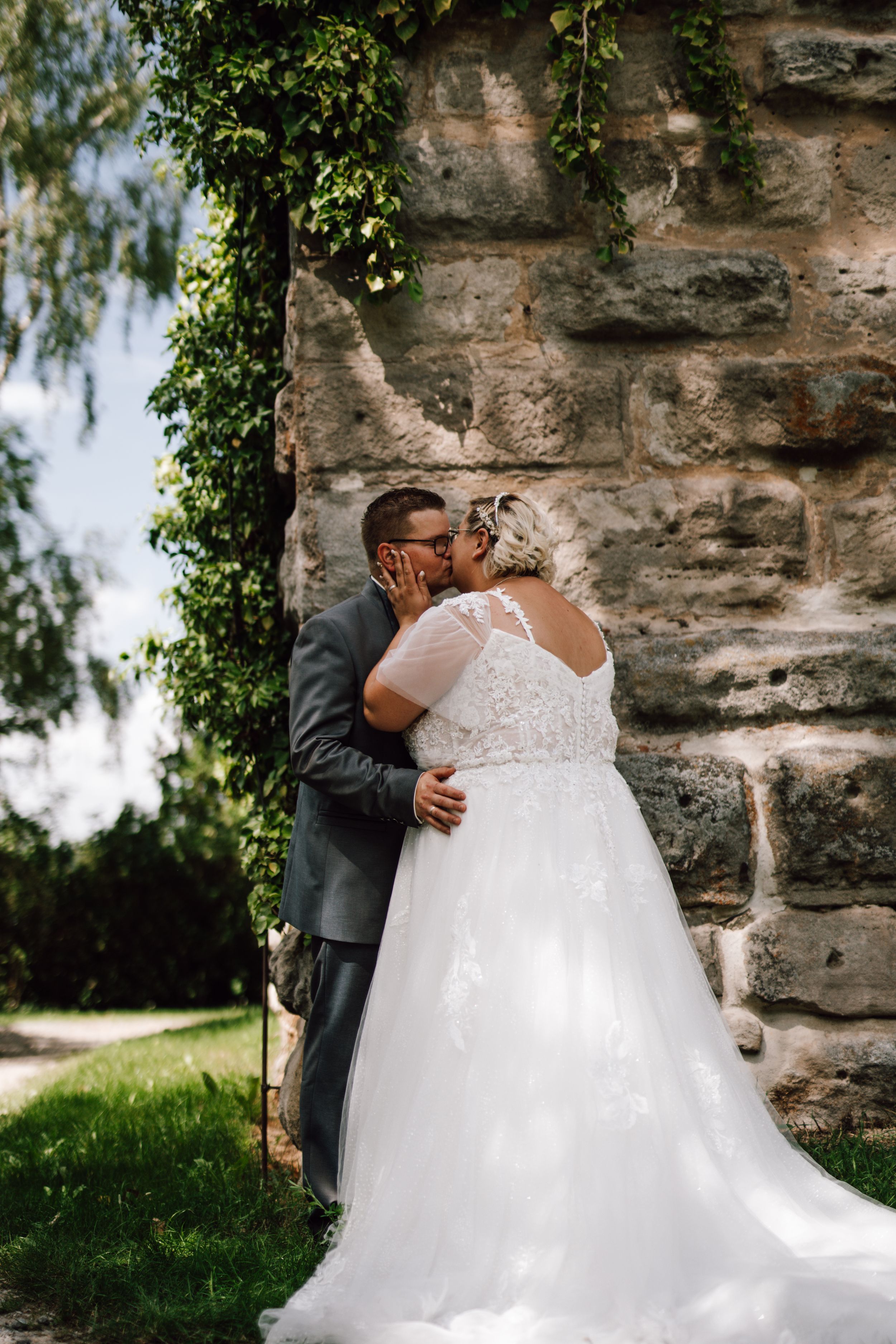 A romantic moment between newlyweds against a stone wall covered in ivy.