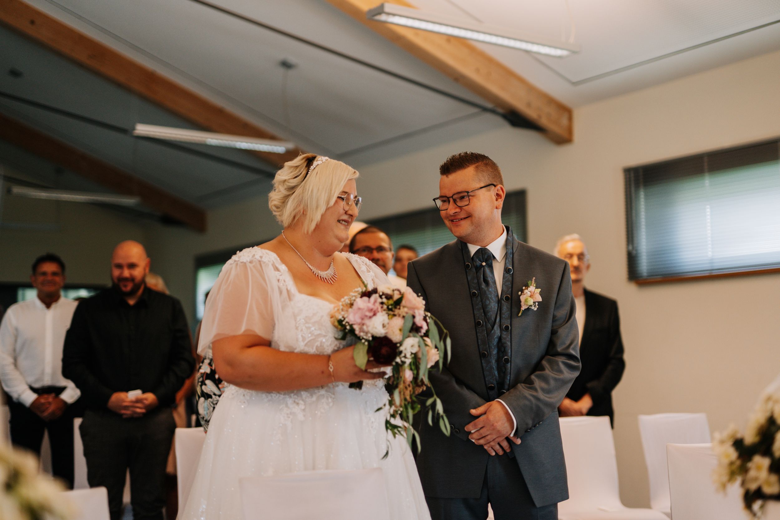 Wedding ceremony with couple standing at altar decorated with white flowers and wooden beams.