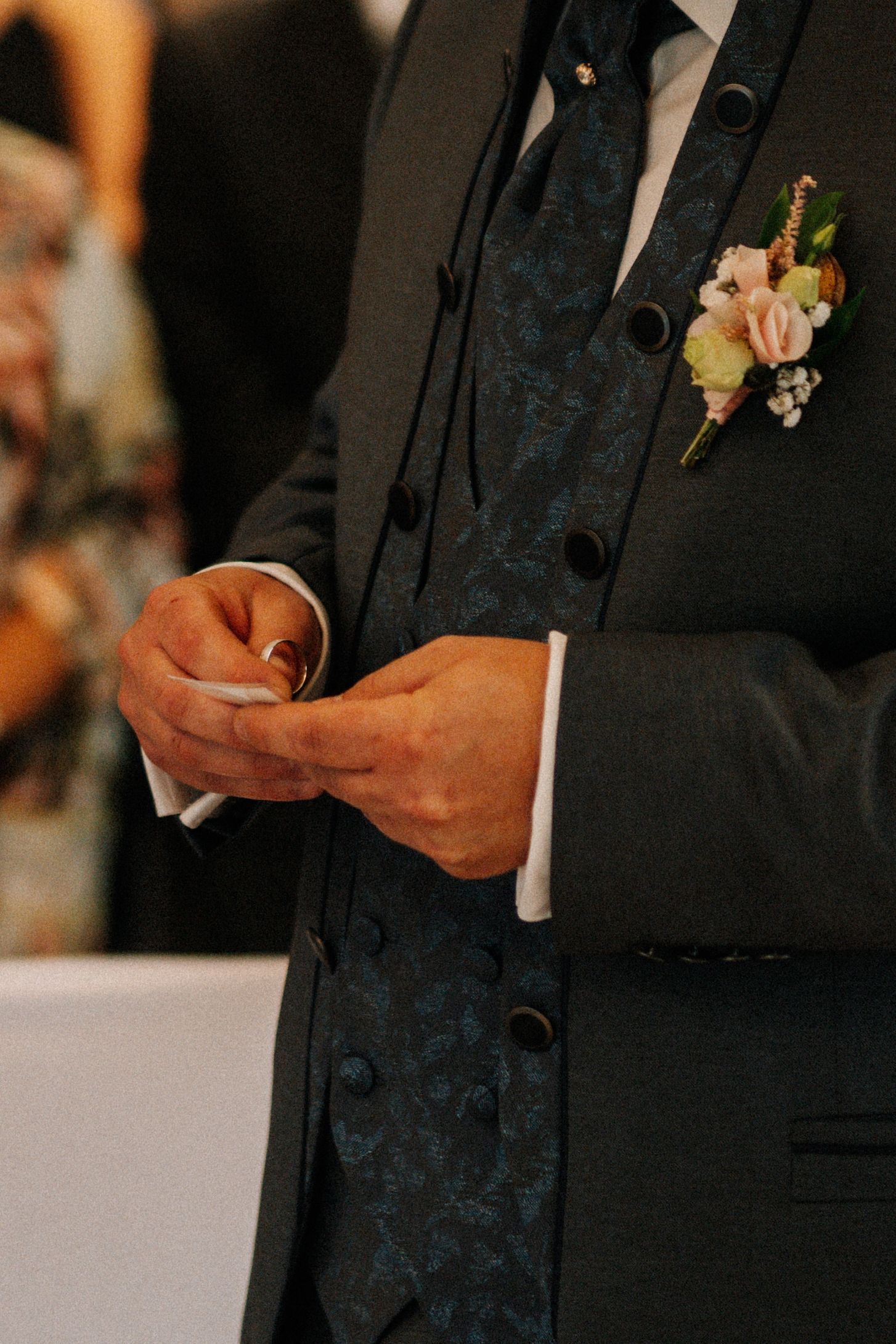 Close up of groom's hands holding ring with boutonniere on lapel.