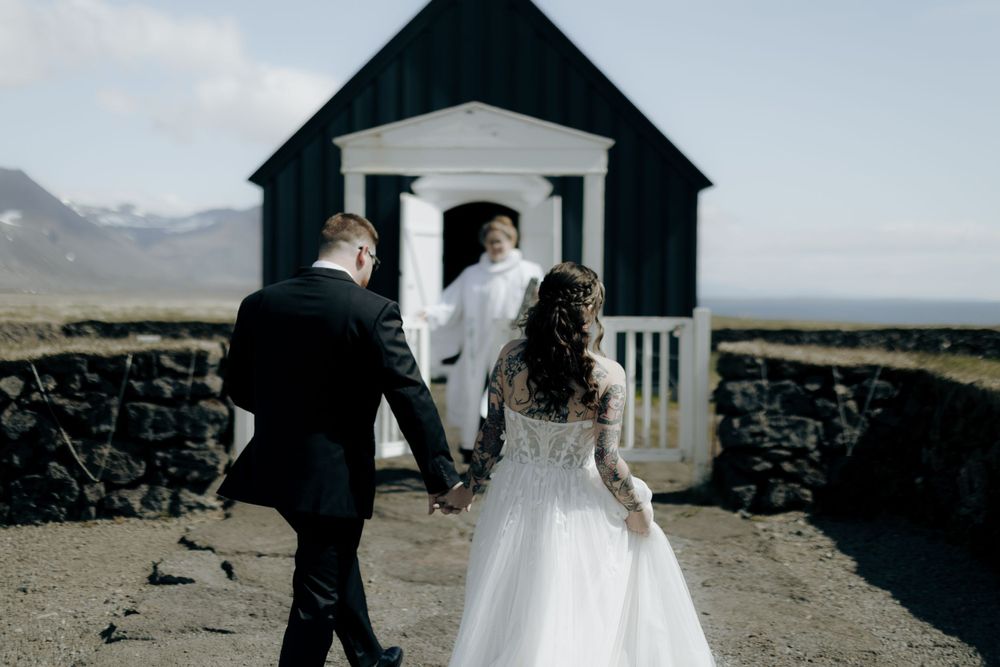 Wedding couple standing outside a small white chapel with stone walls.