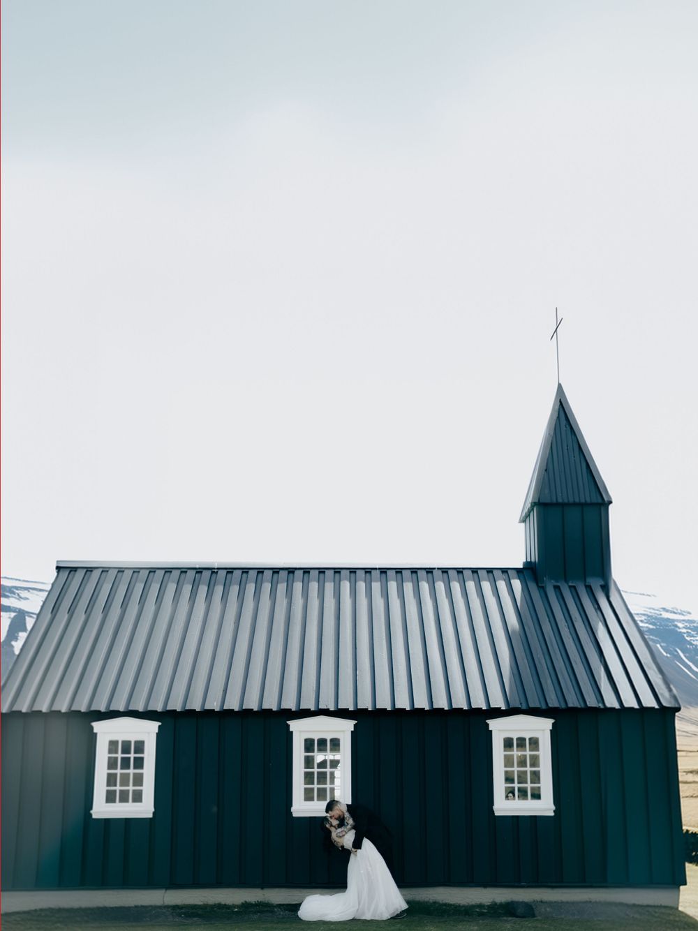 Black church building with white windows against cloudy sky.