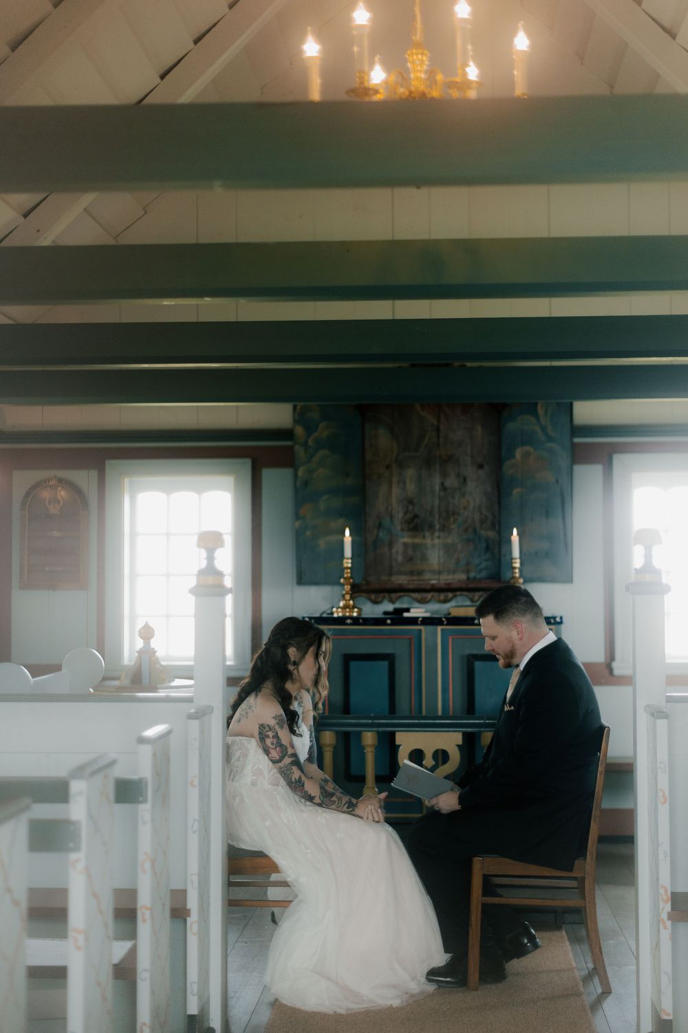 Wedding ceremony in a rustic church with hanging pendant lights and wooden beams.